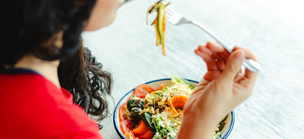 A woman in a red shirt enjoys a fresh salad indoors at a restaurant table.
