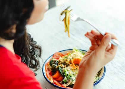 A woman in a red shirt enjoys a fresh salad indoors at a restaurant table.